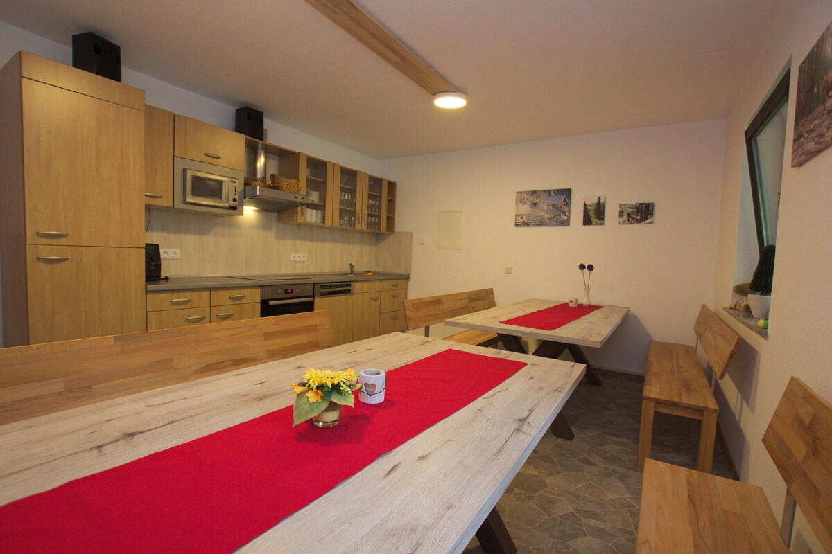 A kitchen with wooden cabinets, a microwave, and a dining area with benches and a table.