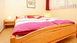 Un letto di legno con una coperta rosa, un comodino con una lampada e un quadro appeso al muro.