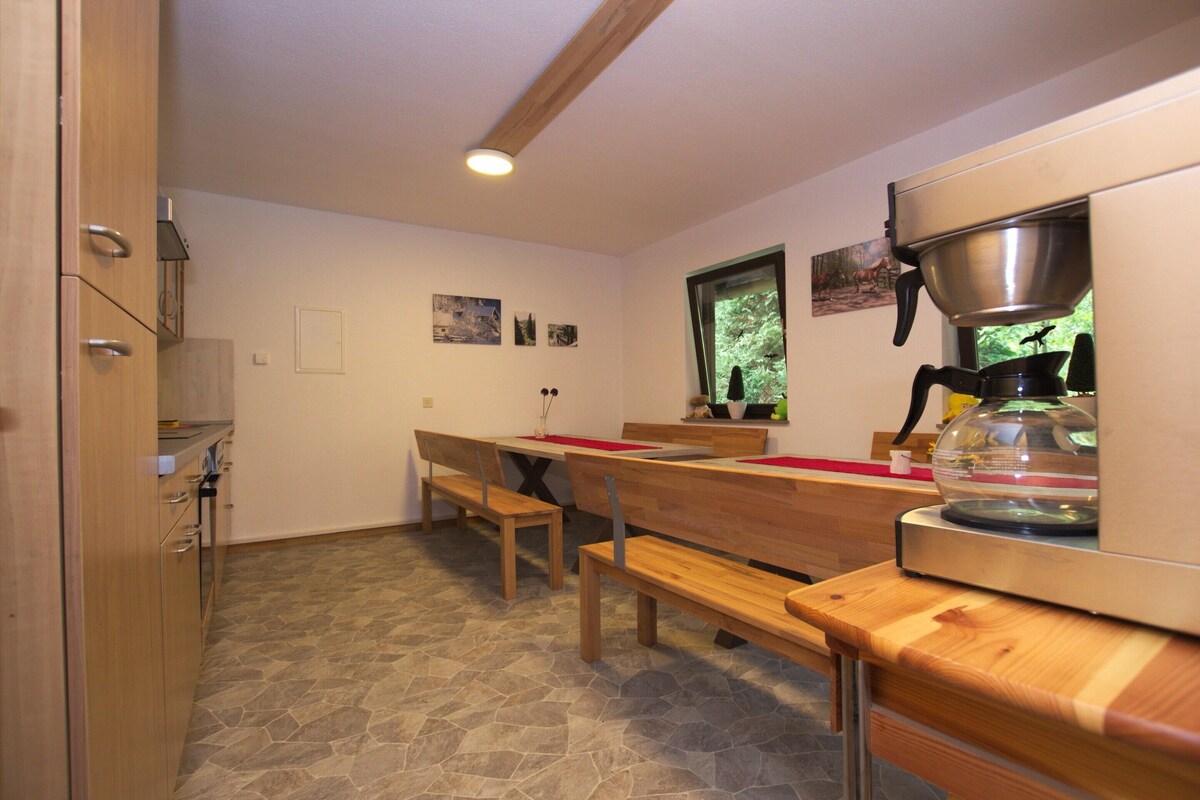A kitchen with wooden benches, a coffee machine, and a window with a view of trees.