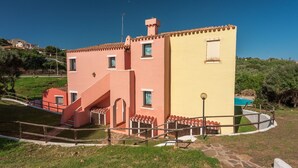 A two-story building with a red and yellow facade, a staircase, and a pool in the background.