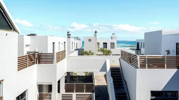 A modern building with white facades and wooden balconies overlooking a coastal area.