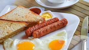 Un plato de desayuno con tostadas, salchichas y huevos fritos, acompañado de una taza de café y salsas.