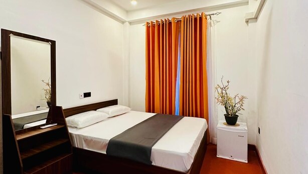 Una habitación de hotel con una cama, un ventilador de techo, aire acondicionado, un espejo y una mesita con una planta.