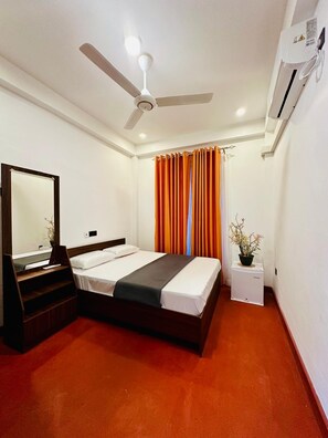 A hotel room with a bed, a ceiling fan, an air conditioner, a mirror, and a small table with a plant. - Tgarden resort (Ella)