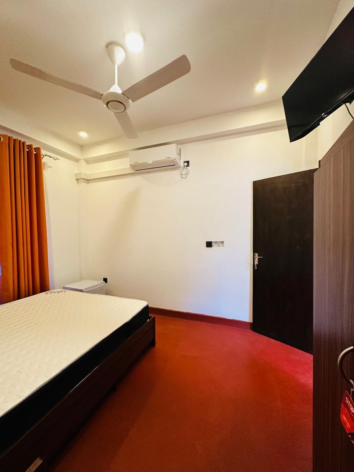 A hotel room with a bed, a ceiling fan, an air conditioning unit, a wardrobe, and a door.