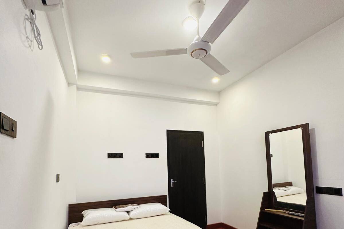 A bedroom with a bed, a ceiling fan, a mirror, and a door.