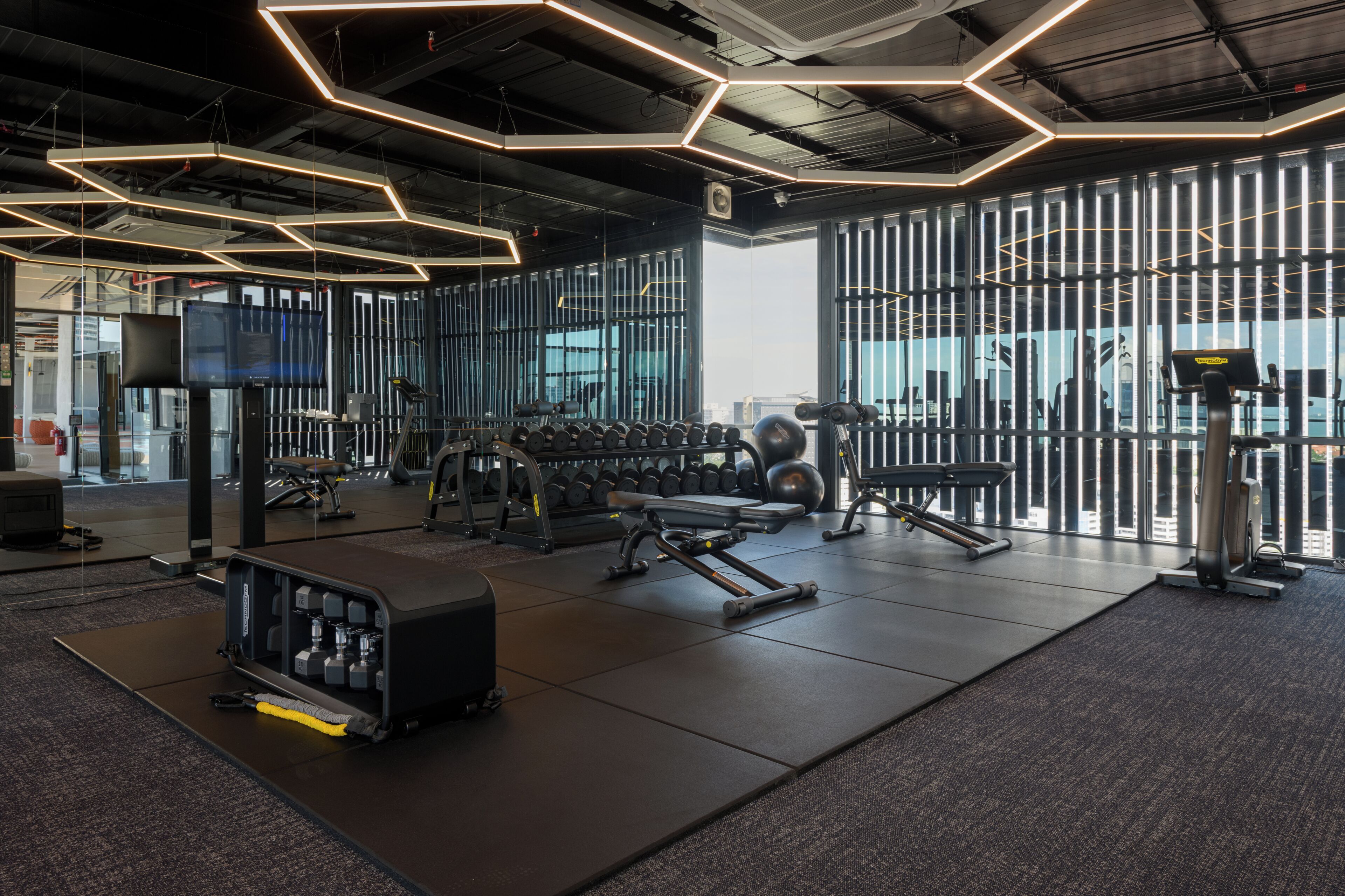 Un gimnasio con equipo de ejercicio, una televisión y ventanas amplias.