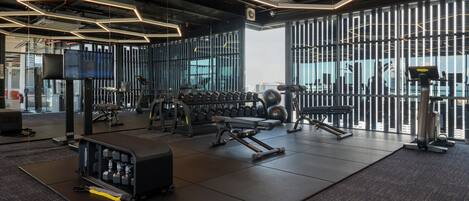 A gym with exercise equipment, a television, and large windows.