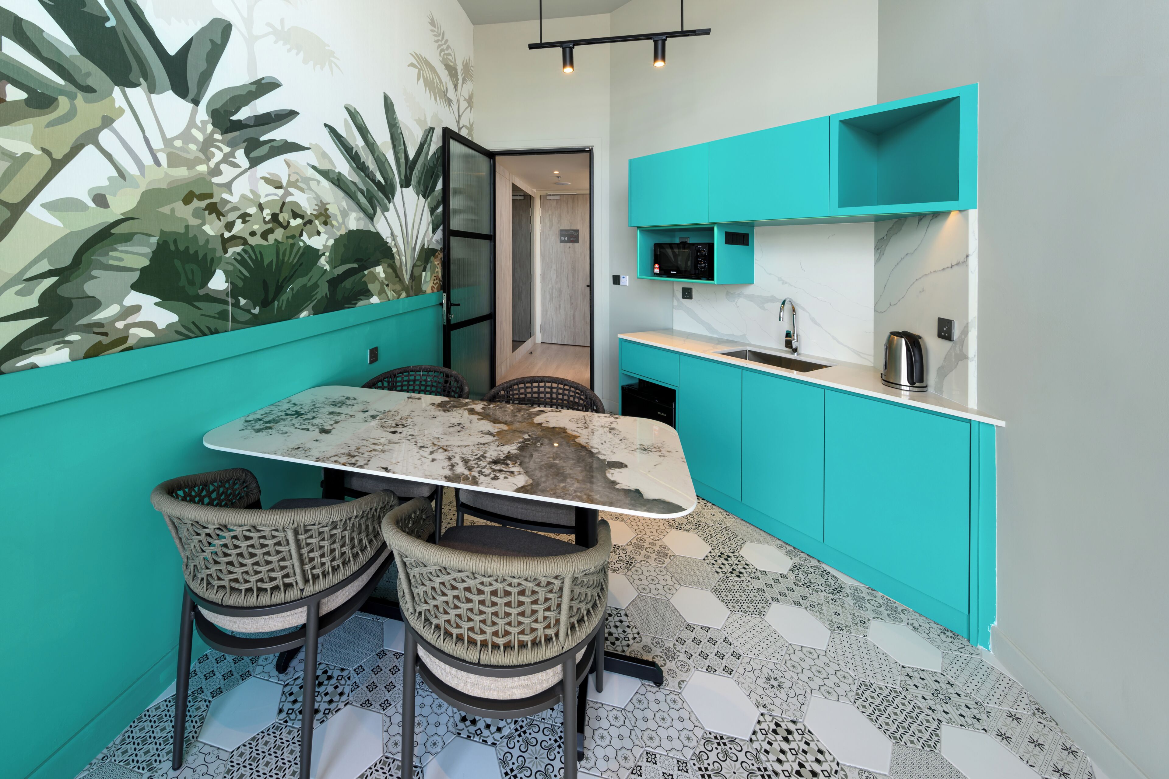 A compact kitchen with teal cabinetry, a marble countertop, and a dining table with four chairs.