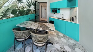 A compact kitchen with teal cabinetry, a marble countertop, and a dining table with four chairs. - Fifth Avenue Hotel (George Town)
