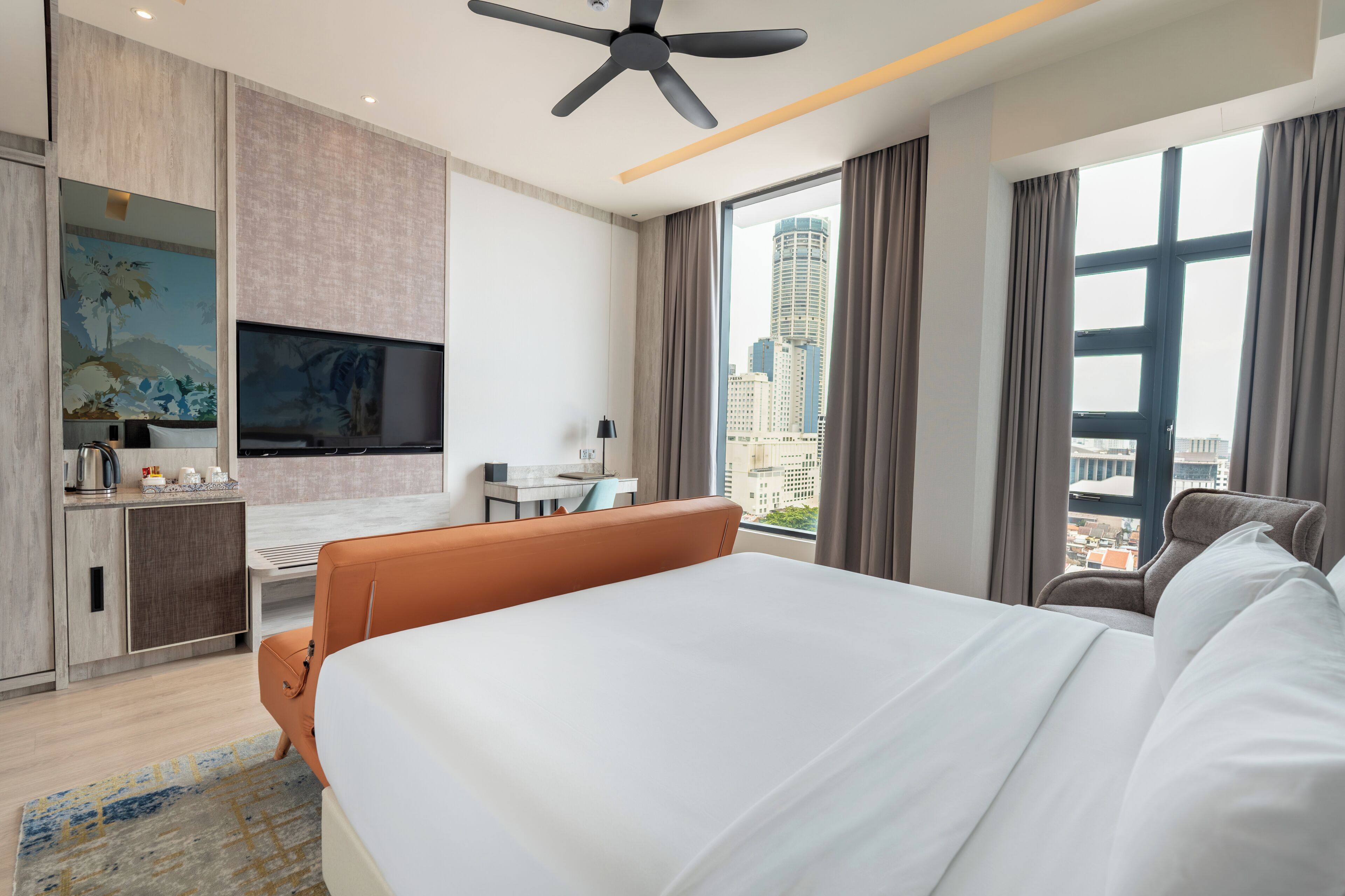 A hotel room with a bed, a desk, a TV, and a view of the city.