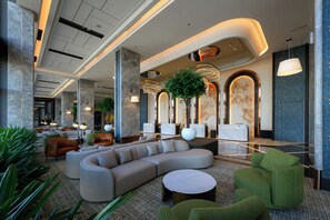 A modern lobby with a curved reception desk, seating areas, and a large plant. - Fifth Avenue Hotel (George Town)