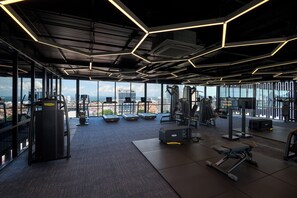 Une salle de sport équipée de matériel d’exercice, dotée de grandes fenêtres et offrant une vue sur la ville.