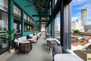 A modern indoor balcony with seating and potted plants, overlooking a cityscape. - Fifth Avenue Hotel (George Town)