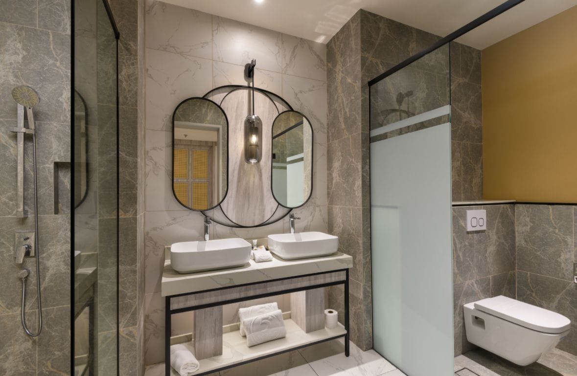 Un baño moderno con ducha envuelta en vidrio, dos lavamanos, un inodoro y un tocador con espejo.