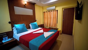 A hotel room with a large bed, wooden headboard, a flat-screen TV, a bedside table with a lamp, and an air conditioning unit. - Benzy Palace Resort (Bhatkal)