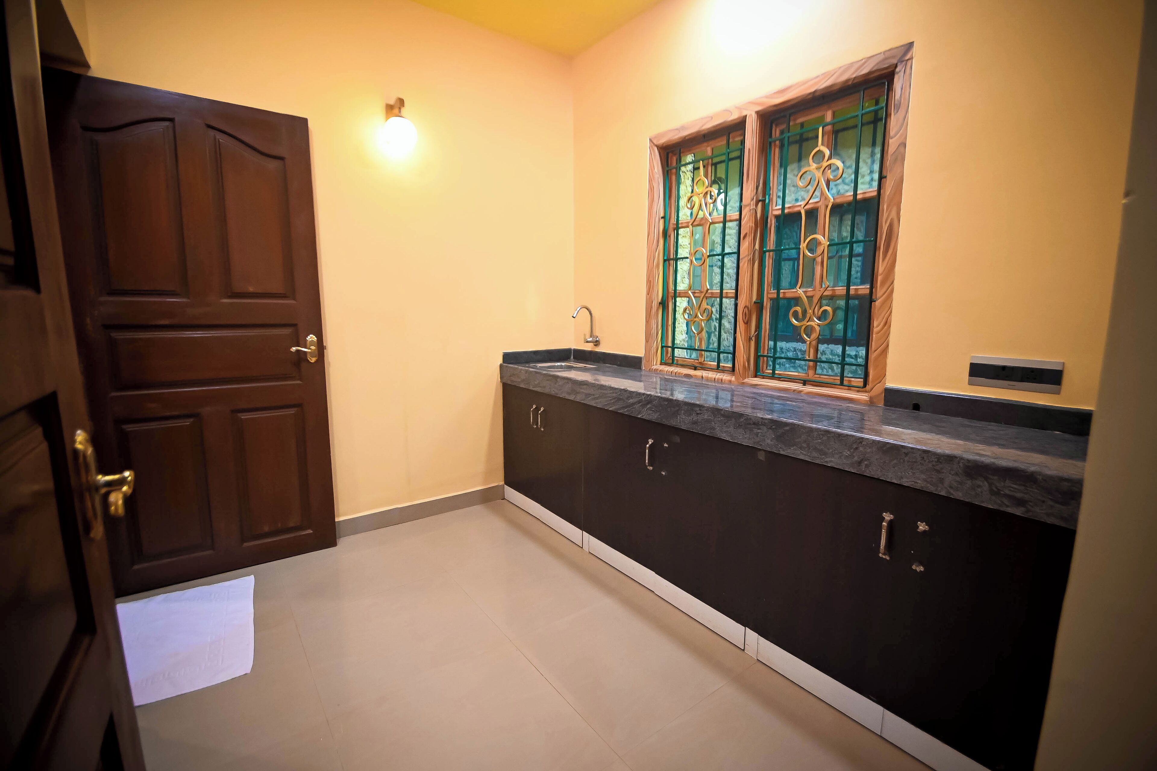 A kitchen with dark cabinets, a marble countertop, a window with decorative bars, and a door with a towel hanging on it.