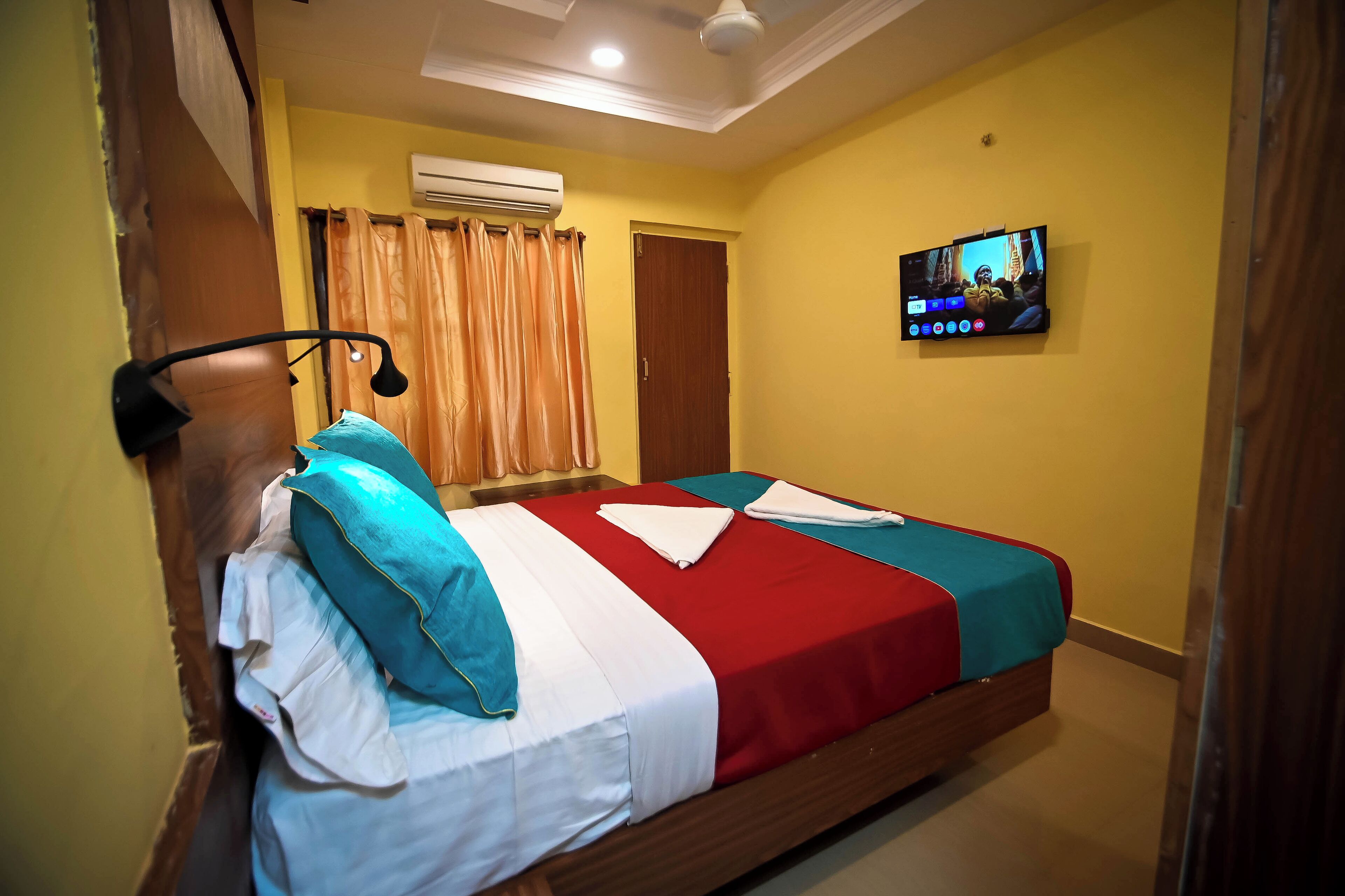 A hotel room with a bed, a TV, and an air conditioning unit.