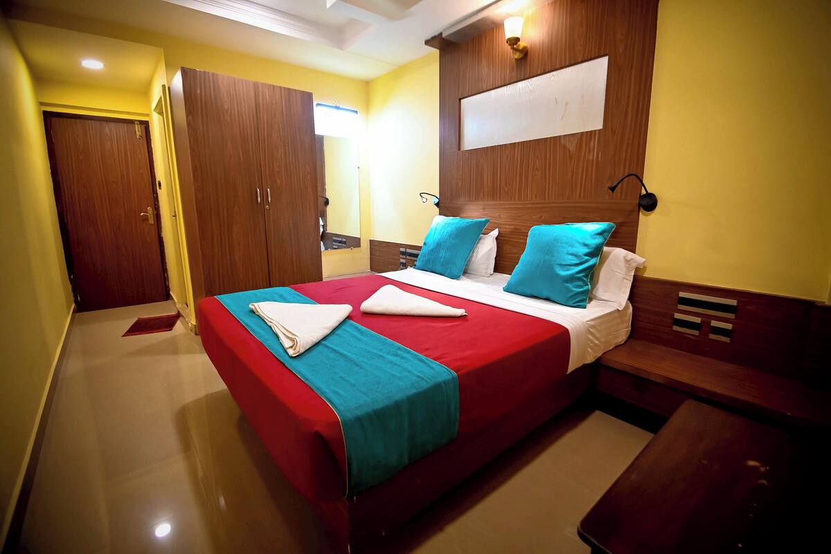 A hotel room with a large bed, wooden headboard, and a red and blue bedspread.
