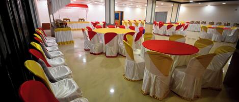 A banquet hall with round tables and chairs, some covered with white and yellow tablecloths, and red and yellow chair covers.