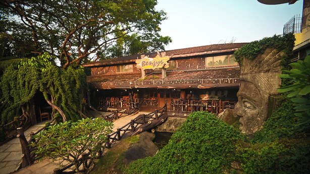 A rustic building with a sign reading "Benny's" and a stone face sculpture. - Benzy Palace Resort (Bhatkal)