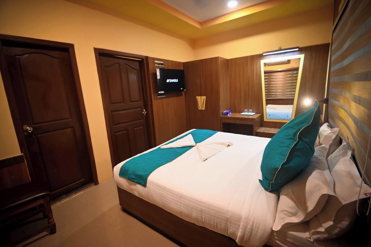 A hotel room with a bed, a television on the wall, and a wooden wardrobe.