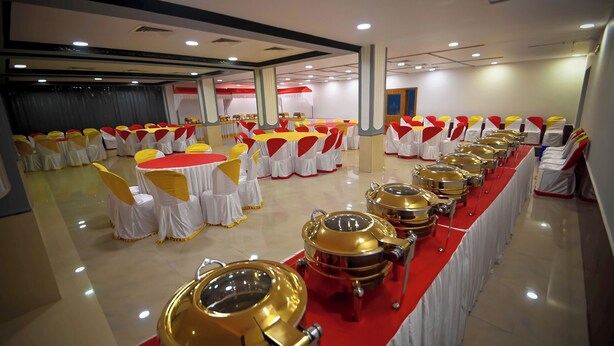 A banquet hall with rows of round tables covered with white tablecloths and yellow sashes, and gold buffet trolleys along the walls. - Benzy Palace Resort (Bhatkal)