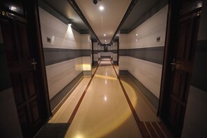 A long, narrow hallway with a shiny floor, flanked by walls with horizontal stripes and doors on both sides. - Benzy Palace Resort (Bhatkal)