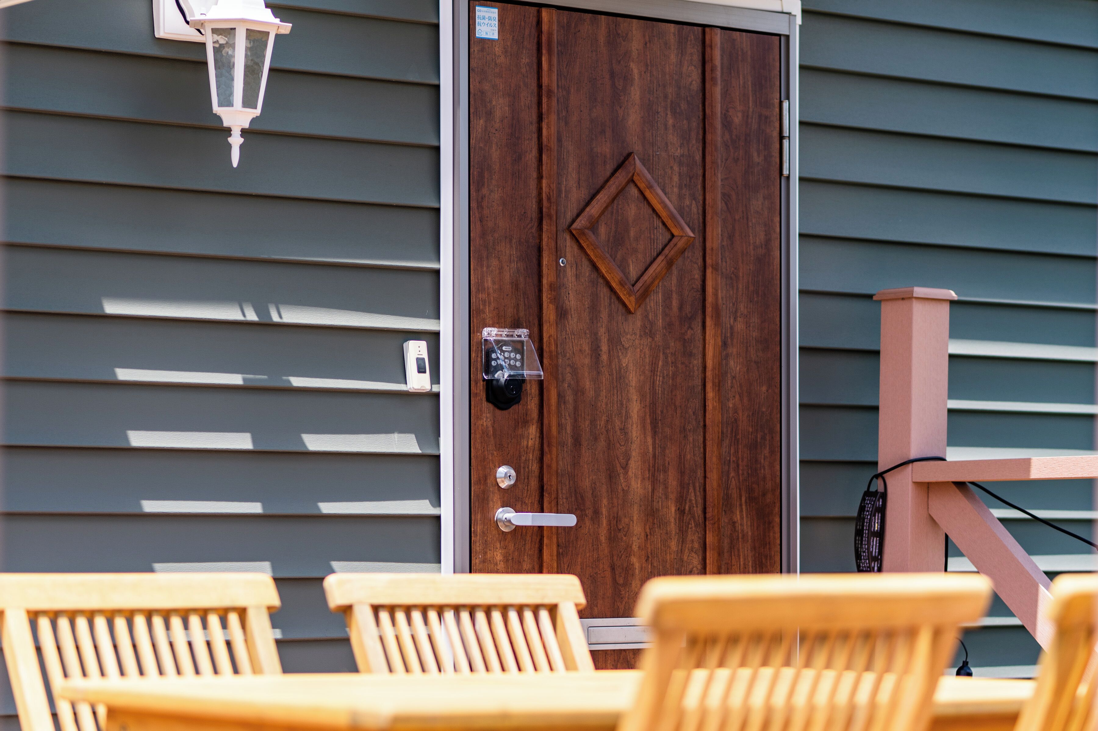 A wooden door with a keypad lock, a mailbox, and a porch with wooden chairs.