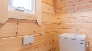 A wooden-paneled bathroom with a toilet, a window, and a wall-mounted electrical outlet.
