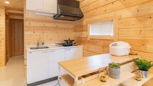A wooden cabin interior with a kitchen featuring a stove, sink, and a rice cooker. - Solana Kamogawa (Kamogawa)