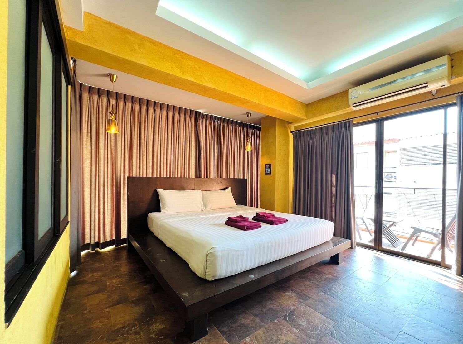 Ein modernes Hotelzimmer mit einem großen Bett, einer Schiebeglastür zum Balkon und einer Klimaanlage an der Wand.