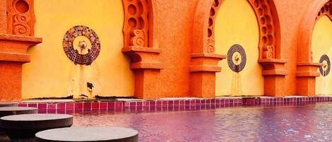 A pool with a geometric design, surrounded by arches with circular cutouts.