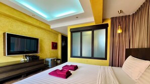 A hotel room with a bed, a TV, a desk with a computer, and a window with curtains. - Le Bush (Pattaya)