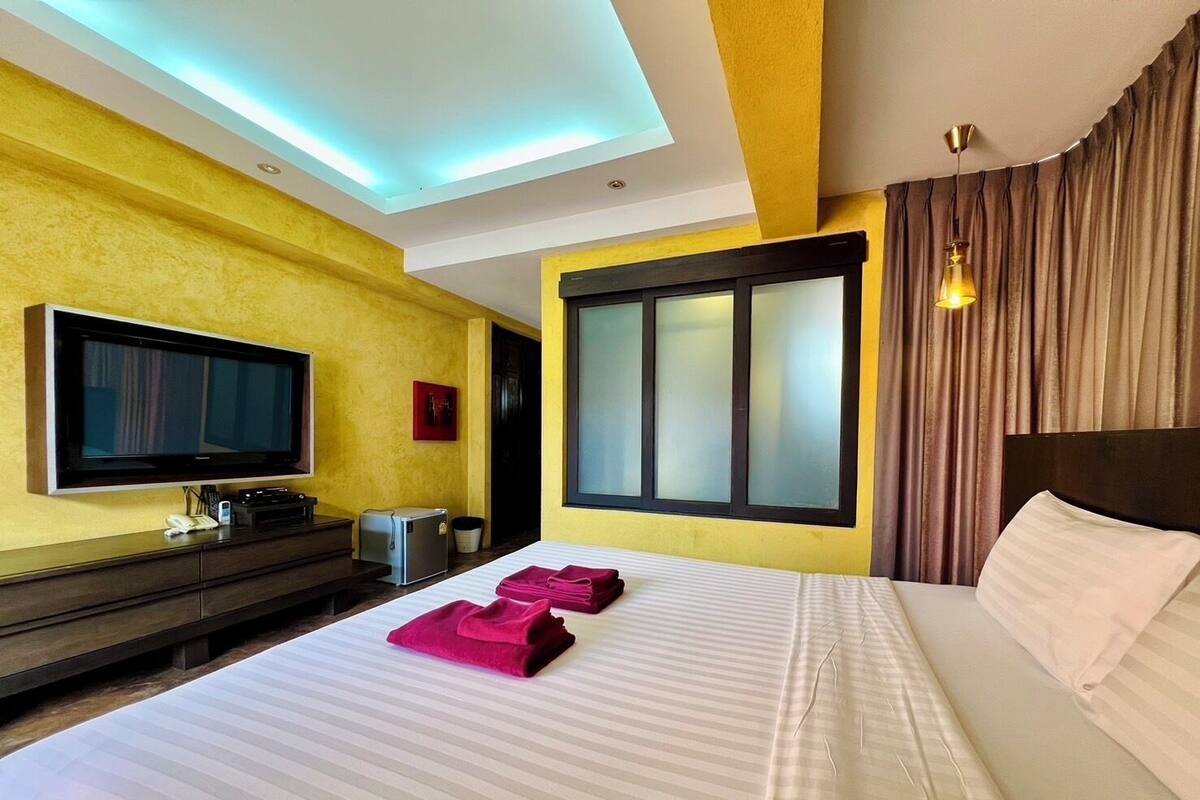 A hotel room with a bed, a TV, a desk with a computer, and a window with curtains.