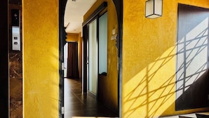 A hotel hallway with a checkered floor, a yellow wall, and a door with a light fixture. - Le Bush (Pattaya)