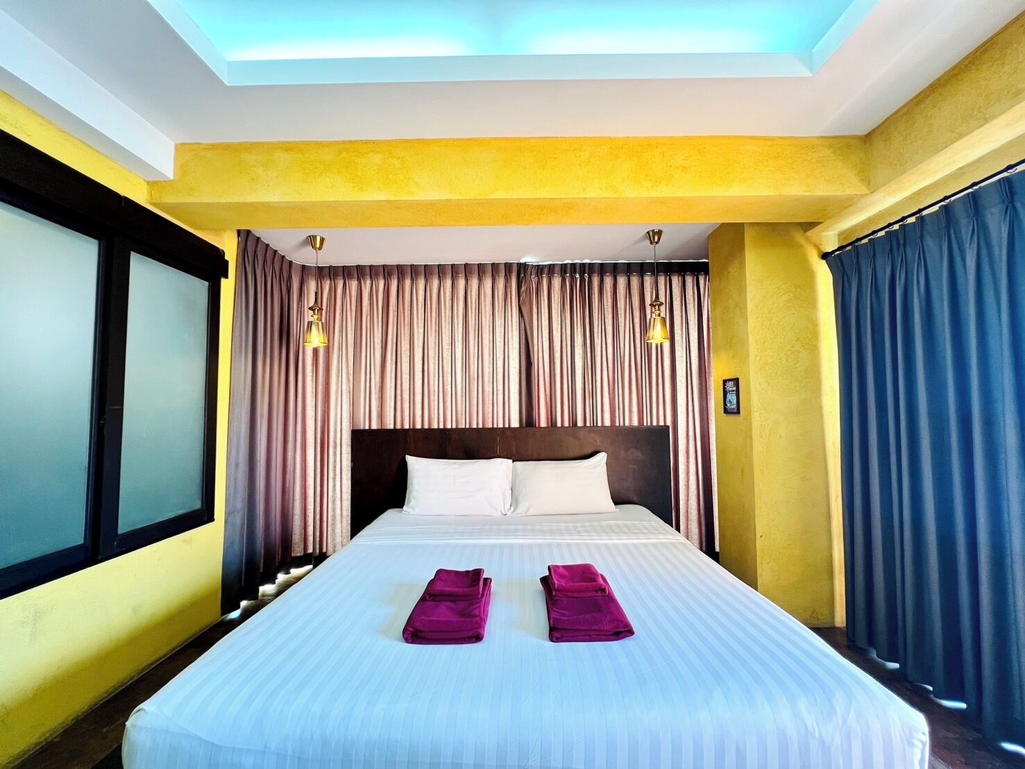 Hotelkamer met een groot bed, twee kussens, een hoofdeinde, een raam met gordijnen en een plafondlamp.