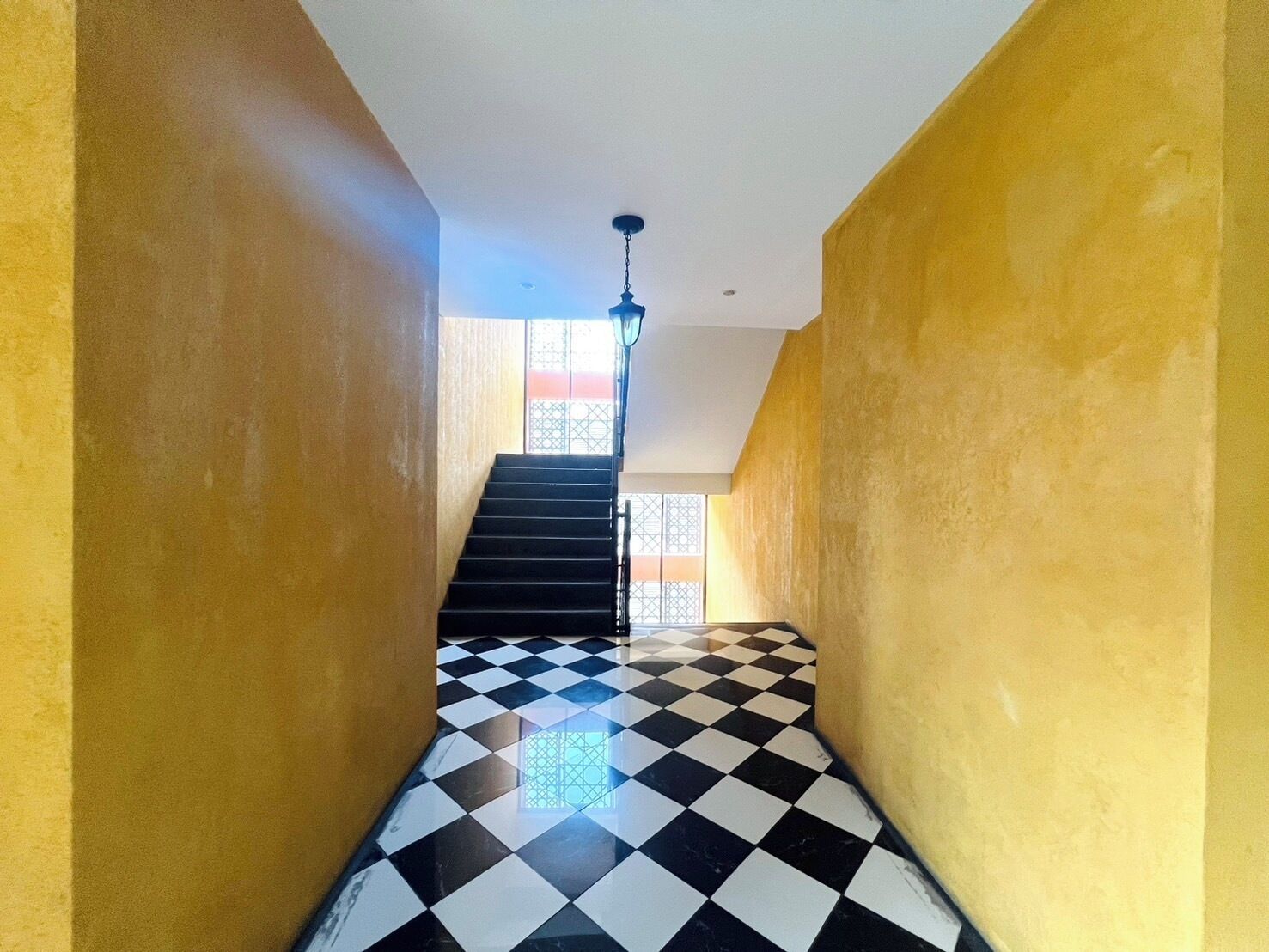 A staircase with black and white checkered flooring leading to a landing with a view of a building outside.