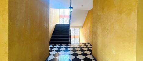 A staircase with black and white checkered flooring leading to a landing with a view of a building outside.