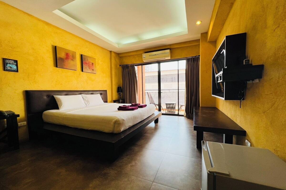 A hotel room with a bed, a desk, a TV, and a balcony with curtains.