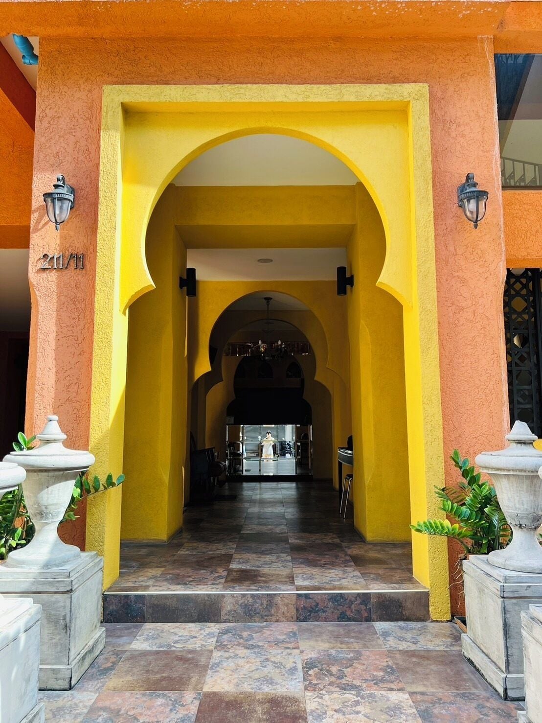 A hotel entrance with a yellow archway, a tiled floor, and two stone planters.