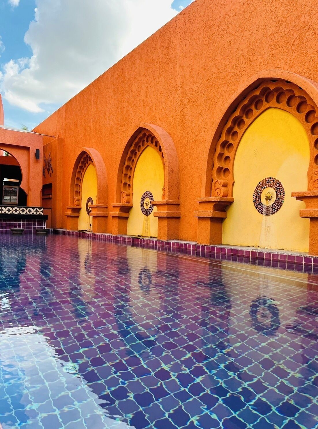 A swimming pool with a tiled floor and archways with circular designs.