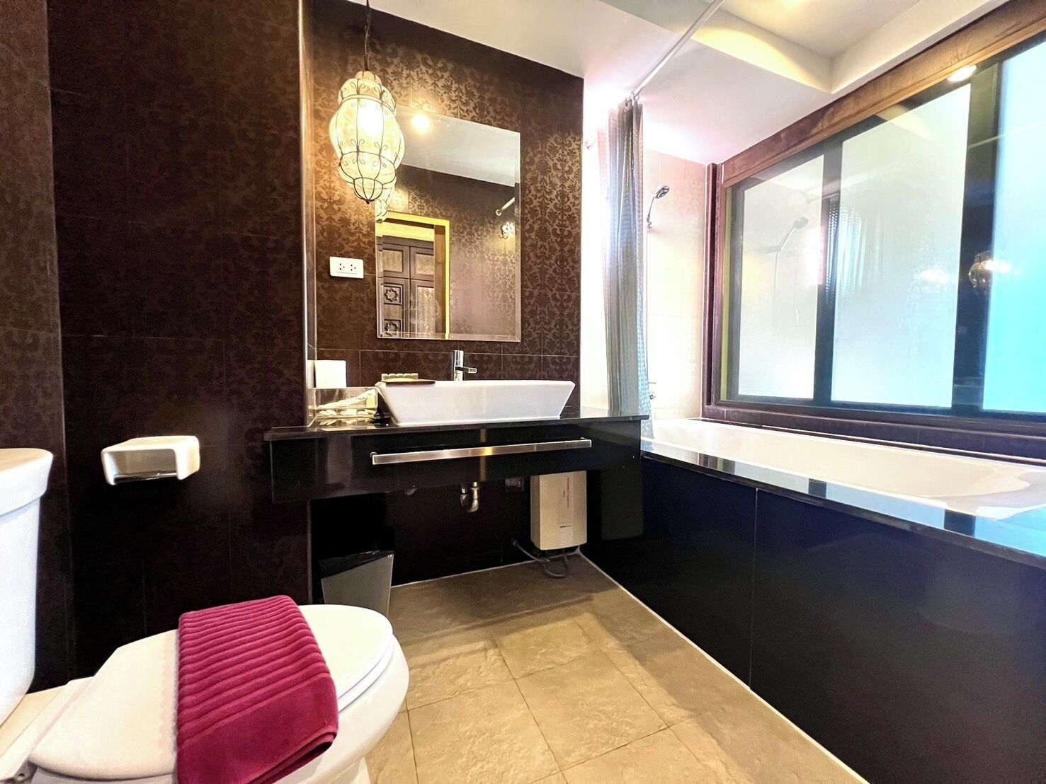 A modern bathroom with a white toilet, a black vanity with a white sink, a large mirror, and a window providing natural light.