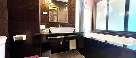 Un baño moderno con inodoro blanco, tocador negro con lavamanos blanco, un espejo grande y una ventana que proporciona luz natural.