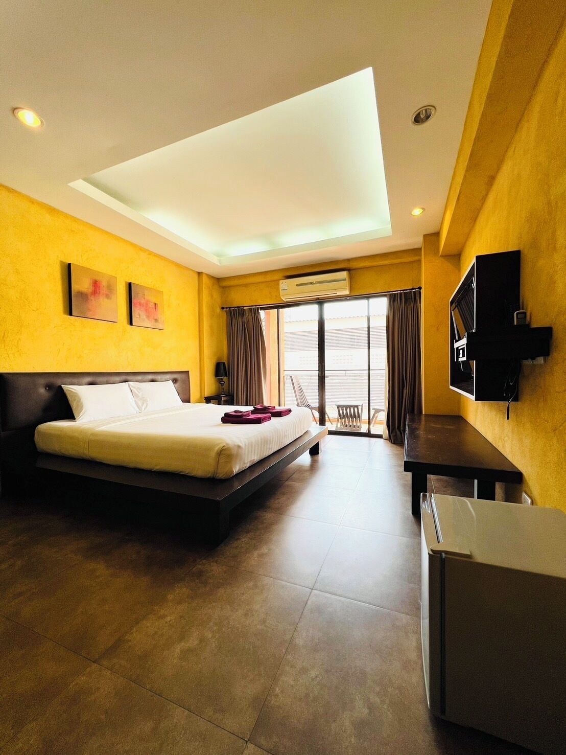 Una habitación de hotel con cama, escritorio, televisión y aire acondicionado.
