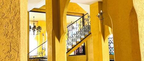 Un interior con paredes amarillas, una escalera y un ventanal con rejas decorativas de hierro.