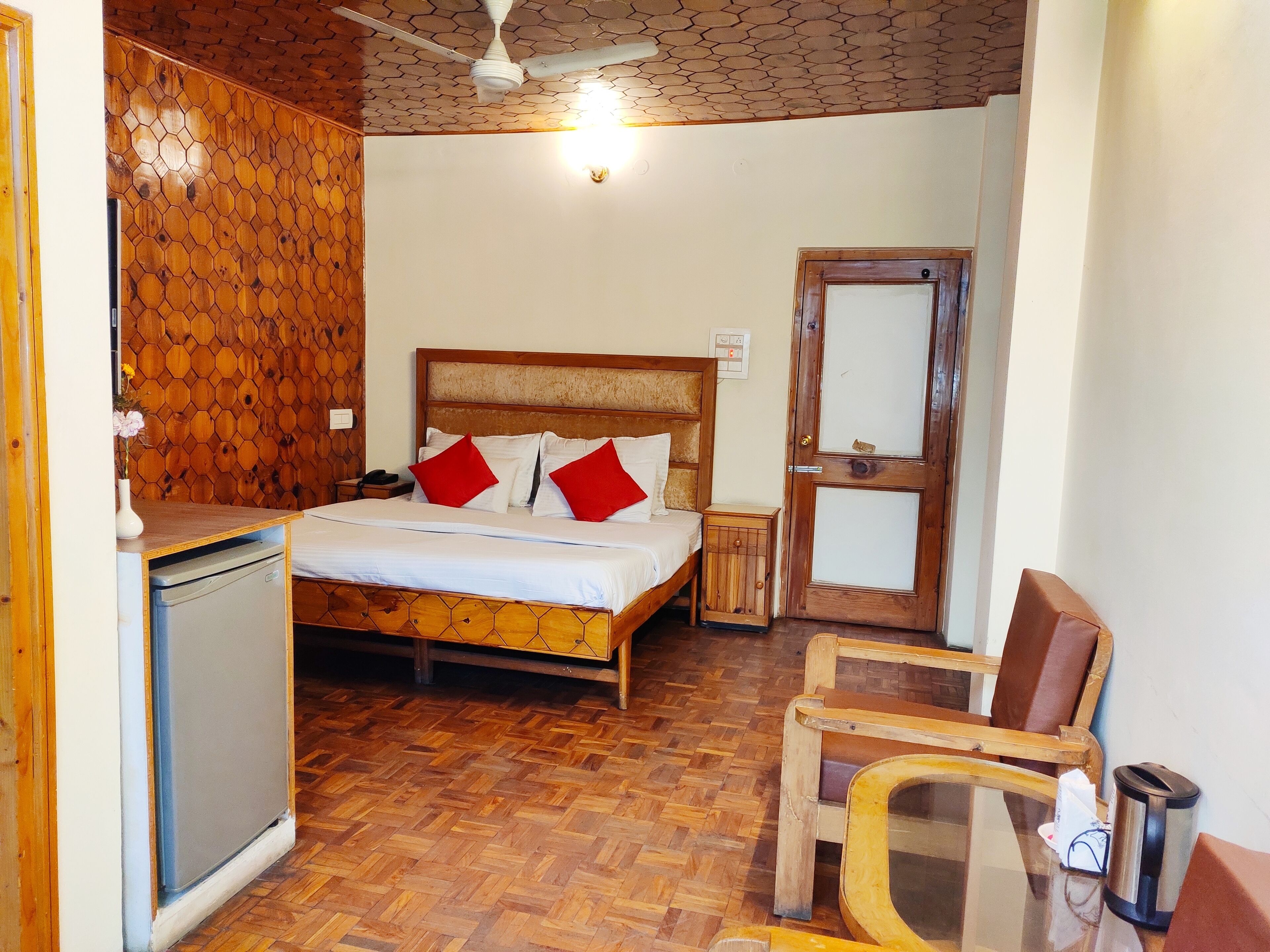 A bedroom with a wooden bed, a nightstand, a small wooden cabinet, a chair, and a refrigerator.