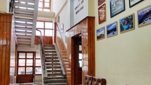 A lobby with a staircase, wooden benches, a reception desk, and framed pictures on the wall. - HimalayanHamlet ValleyView (Kullu)