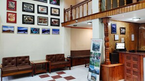 A lobby with a wooden reception desk, two leather sofas, a bulletin board with framed pictures, and a staircase. - HimalayanHamlet ValleyView (Kullu)