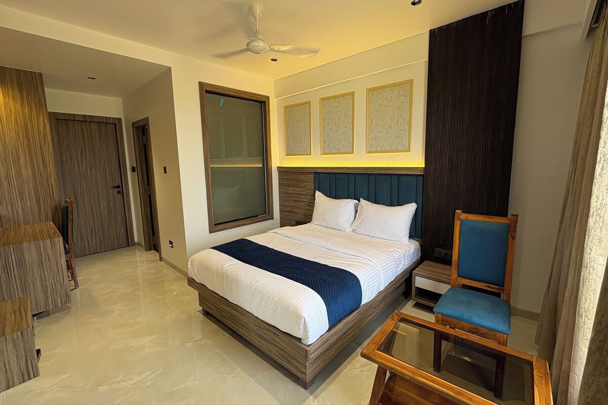 A modern hotel room with a large bed, a glass coffee table, a chair, a ceiling fan, and a view of the outside.